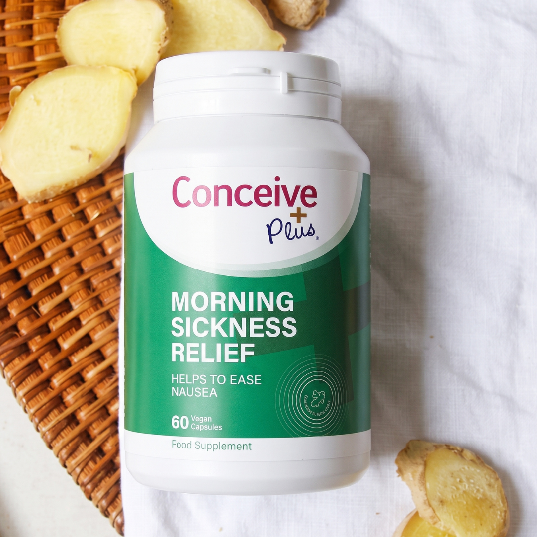 A bottle of Conceive Plus Morning Sickness Relief dietary supplement placed on a white fabric surface next to sliced ginger and a woven basket.