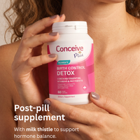 A woman holds a white bottle of Conceive Plus Birth Control Detox dietary supplement. The bottle features a pink and white label.