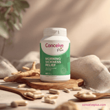 Conceive Plus morning sickness relief supplement bottle on a wooden surface with scattered pills.